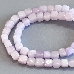 Pu&ograve; includere: Un filo di perline lisce a forma di cubo color lavanda chiaro. Ogni perlina presenta una finitura lucida con sottili variazioni di tono e opacit&agrave;, disposte in un anello continuo per mostrare la forma quadrata uniforme e la tonalit&agrave; viola.