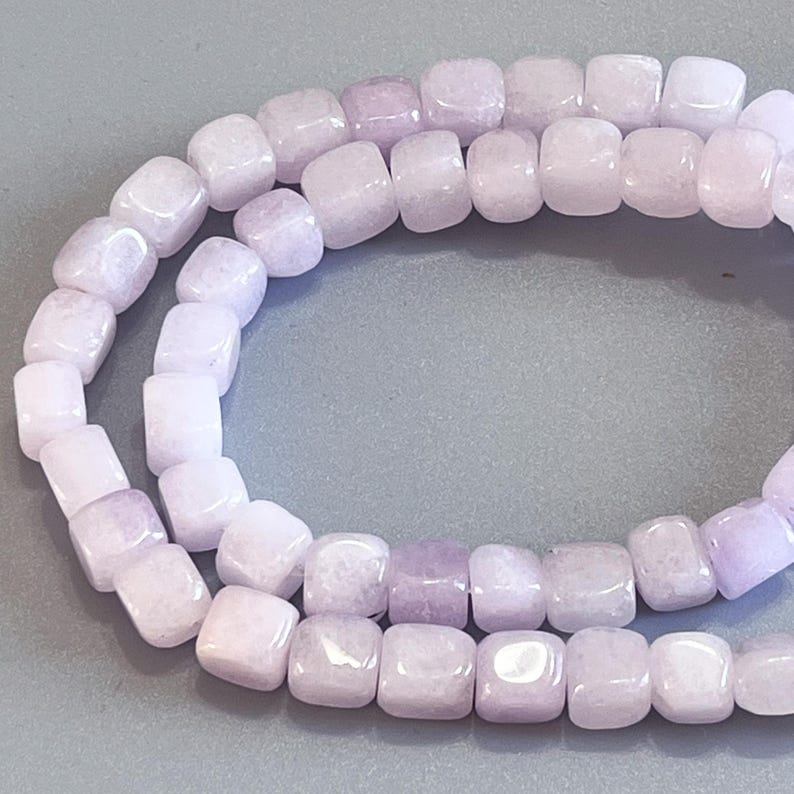 Pu&ograve; includere: Un filo di perline lisce a forma di cubo color lavanda chiaro. Ogni perlina presenta una finitura lucida con sottili variazioni di tono e opacit&agrave;, disposte in un anello continuo per mostrare la forma quadrata uniforme e la tonalit&agrave; viola.