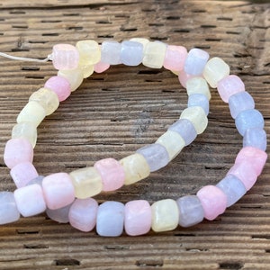 Peut inclure: Un collier de perles carr&eacute;es de couleur pastel. Les perles sont dans les tons de rose, de jaune et de bleu. Les perles sont enfil&eacute;es sur une fine ficelle blanche. Le fond est une surface en bois vieilli.