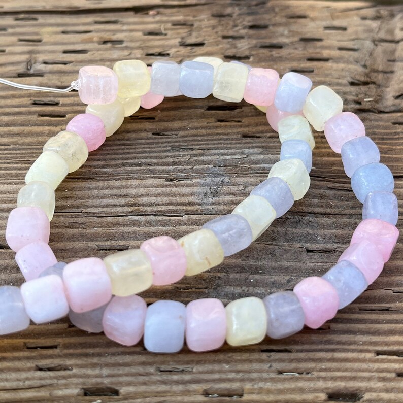 Peut inclure: Un collier de perles carr&eacute;es de couleur pastel. Les perles sont dans les tons de rose, de jaune et de bleu. Les perles sont enfil&eacute;es sur une fine ficelle blanche. Le fond est une surface en bois vieilli.
