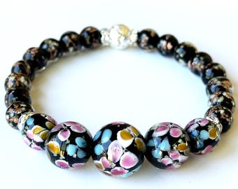 Può includere: Un braccialetto di perline di vetro nero con motivi floreali colorati. Il braccialetto include perline focali più grandi con accenti rosa, blu e gialli e una chiusura argentata. Le perline hanno un diametro di circa 1,3 cm.