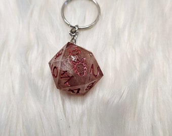 May include: A pink and silver glitter resin d20 dice keyring with a red dragon design. The keyring is attached to a silver metal ring.