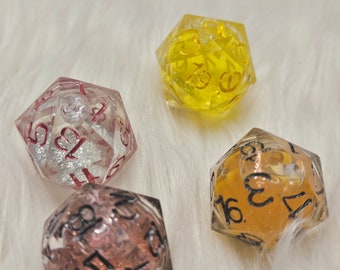 May include: Four clear resin dice with glitter and different coloured resin. The dice are numbered 1-6, 1-20, 1-8, and 1-12. The dice are on a white fluffy surface.