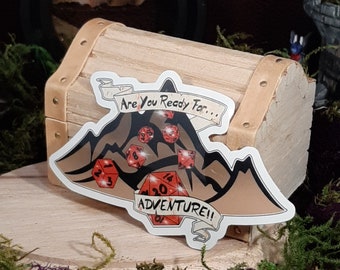 May include: A sticker featuring a mountain range with dice rolling down the slopes. The sticker says "Are you ready for... Adventure!"