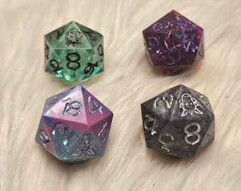 May include: Four multi-sided dice in different colours. One is green with black numerals, another is purple with purple numerals, a third is blue and pink with silver numerals, and the last is grey with silver numerals.
