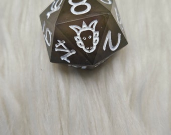 May include: A dark grey, multi-sided dice with white numbers and a dragon symbol. The dice is a D20, with numbers 1 through 20.