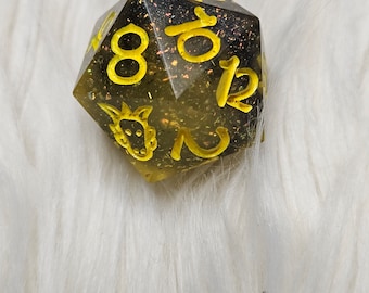 May include: A black and yellow 12-sided dice with glitter embedded in the resin. The dice has yellow numbers and a dragon symbol.