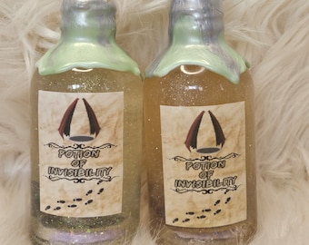 May include: Two glass bottles filled with a shimmering, golden liquid, labelled "Potion of Invisibility." Each bottle has a silver and green wax seal and a crystal-like stopper. The labels feature a stylized design and footprints.