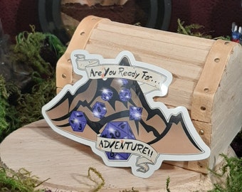May include: A sticker featuring a mountain range design with a banner that reads "Are you ready for... Adventure!" with purple dice scattered on the mountain.