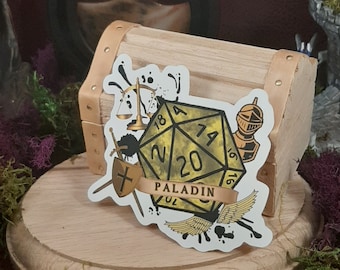 May include: A white sticker featuring a black and gold 20-sided die with the word "PALADIN" on it. The die is surrounded by a scale, a sword, a winged helmet, and wings.