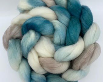 Può includere: Primo piano di un nastro intrecciato nei toni del blu, verde acqua, crema e talpa. La fibra di lana è disposta a cerchio, con ogni filo ben visibile. Il nastro è morbido e soffice.