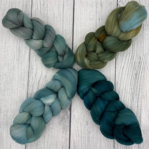 Può includere: Quattro fasci intrecciati di morbida lana cardata disposti a forma di X. Il fascio in alto a sinistra è verde salvia tenue, quello in alto a destra è un mix di oliva e ottanio, quello in basso a sinistra è blu schiuma di mare e quello in basso a destra è ottanio scuro.