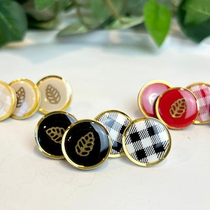 May include: Five gold-rimmed earrings with different designs. Two earrings feature a black and white checked pattern, one earring has a red base with a gold leaf design, and two earrings have a black base with a gold leaf design.