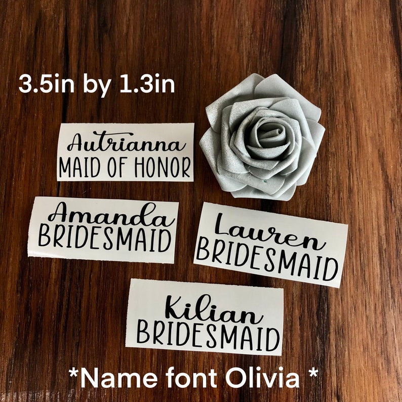 Peut inclure: &Eacute;tiquettes nominatives en vinyle blanc avec texte noir, dont "Autrianna MAID OF HONOR", "Amanda BRIDESMAID", "Lauren BRIDESMAID" et "Kilian BRIDESMAID". Une rose en tissu argent&eacute; est &eacute;galement pr&eacute;sente. Les &eacute;tiquettes mesurent 8,9 cm sur 3,3 cm.