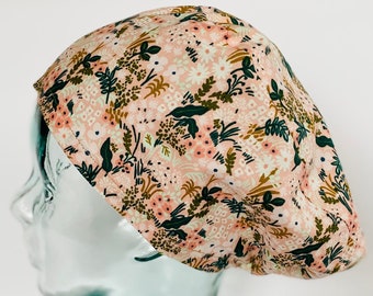 Puede incluir: Un gorro de quirófano de color rosa y verde con estampado floral. El gorro está en una cabeza de maniquí de vidrio.