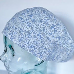 May include: A white scrub cap with a blue floral pattern. The cap is made of a soft, comfortable fabric and is perfect for nurses, doctors, and other healthcare professionals.