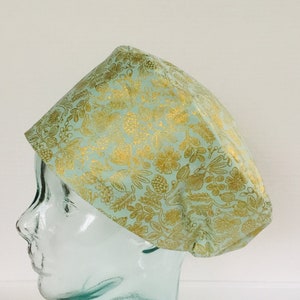 May include: A light blue fabric hat with a gold floral pattern. The hat is on a glass mannequin head.