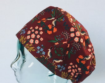 May include: A burgundy scrub hat with a floral pattern featuring small birds and flowers. The hat is made of a soft, comfortable fabric and is perfect for healthcare professionals.