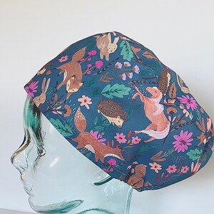 May include: A blue scrub hat with a woodland animal print featuring foxes, rabbits, hedgehogs, and flowers.