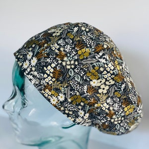 May include: A black scrub cap with a floral pattern featuring white, yellow, and brown flowers. The cap is made of a soft, comfortable fabric and is perfect for keeping hair out of the way while working.