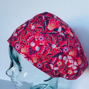 May include: A red floral patterned scrub cap. The cap features a repeating pattern of flowers, leaves, and berries in shades of blue, white, pink, and peach. The cap is designed to be worn in a medical or healthcare setting.