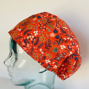 May include: A red scrub cap with a floral pattern featuring white, blue, and green flowers and leaves.