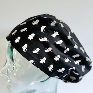 May include: Black surgical scrub cap with a repeating pattern of white cartoon ghosts with red eyes. The cap is made of a soft fabric and is designed to fit comfortably. The cap is a Halloween-themed accessory.