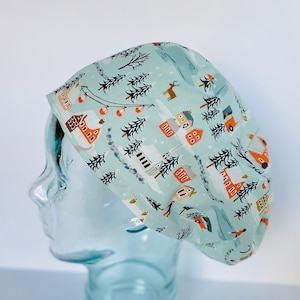 May include: A light blue scrub cap with a winter village pattern. The pattern includes houses, trees, skiers, and reindeer. The cap is made of a soft, lightweight fabric and is designed to fit comfortably.