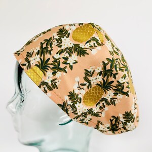 May include: A pink scrub hat with a pineapple and floral print. The hat is made of a soft, comfortable fabric and is perfect for nurses, doctors, and other healthcare professionals.