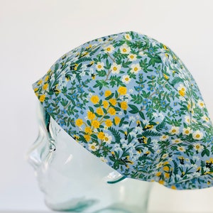 May include: A blue and white floral print scrub hat with yellow flowers. The hat is on a glass head form.