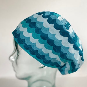 May include: A blue and white patterned surgical scrub hat with a wave design. The hat is on a glass head form.