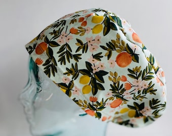 May include: A light blue surgical scrub cap with a floral pattern. The pattern includes yellow lemons, orange fruits, pink flowers, and green leaves. The cap is made of a soft fabric and is designed to cover the head.