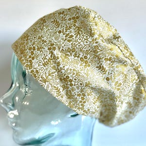 May include: A white scrub hat with a gold floral pattern. The hat is made of a soft, comfortable fabric and is perfect for nurses, doctors, and other healthcare professionals.