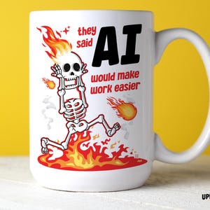 Puede incluir: Una taza de cerámica blanca con el gráfico de un esqueleto con la cabeza en llamas corriendo a través del fuego. El texto dice, they said AI would make work easier. El diseño incluye llamas naranjas y rojas, un esqueleto blanco y texto negro y rojo.