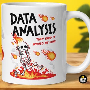 Puede incluir: Taza de cerámica blanca con una ilustración en blanco y negro de un esqueleto en llamas. El texto en la taza dice "Data Analysis They said it would be fun!"