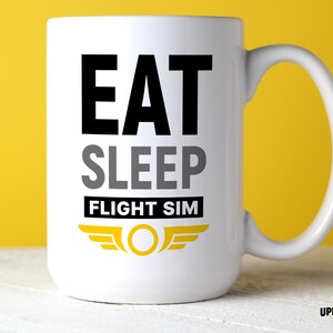 May include: A white ceramic mug featuring the black text EAT, grey text SLEEP, and black text FLIGHT SIM on a white background. Below the text is a yellow graphic of a circle with wings. The mug has a curved handle on the right side.