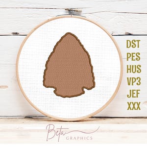 May include: A brown arrowhead design is embroidered on white fabric, framed by a wooden embroidery hoop. The design is surrounded by a brown outline. The image includes the text "DST, PES, HUS, VP3, JEF, XXX" and the "Beta Graphics" logo.