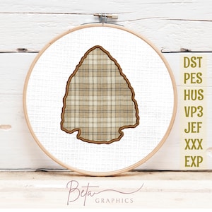 May include: A wooden embroidery hoop holds a white fabric with a plaid arrowhead design. The arrowhead is outlined in brown and filled with a tan and brown plaid pattern. The text "Beta Graphics" is at the bottom.