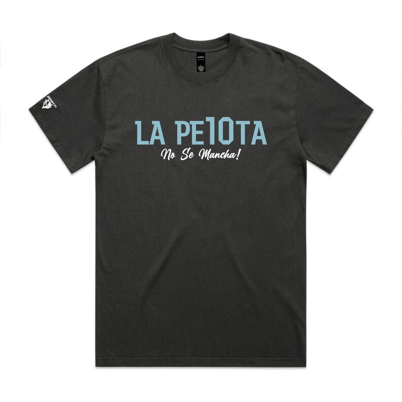 Puede incluir: Camiseta gris oscuro con el texto "LA PELOTA" en azul claro, sobre el texto "No Se Mancha!" en letra cursiva. Un peque&ntilde;o logotipo es visible en la manga izquierda. Es una prenda de vestir informal.