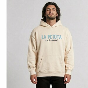 Puede incluir: Sudadera con capucha color crema con bolsillo delantero y capucha. El texto "LA PELOTA No Se Mancha!" est&aacute; impreso en azul claro en el pecho. La sudadera est&aacute; hecha de un material suave.