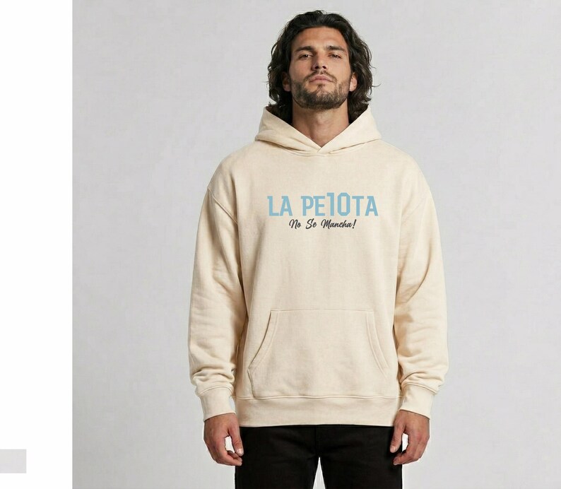 Puede incluir: Sudadera con capucha color crema con bolsillo delantero y capucha. El texto "LA PELOTA No Se Mancha!" est&aacute; impreso en azul claro en el pecho. La sudadera est&aacute; hecha de un material suave.