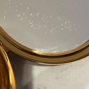 Peut inclure: Un r&eacute;cipient circulaire avec un bord en or m&eacute;tallique et une substance blanche semi-solide &agrave; l'int&eacute;rieur. La surface du mat&eacute;riau blanc pr&eacute;sente une texture subtilement tachet&eacute;e et le bord dor&eacute; offre une finition polie et r&eacute;fl&eacute;chissante.