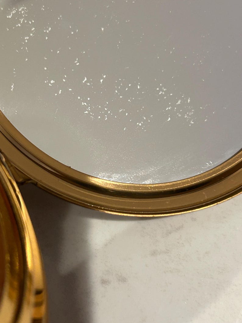 Peut inclure: Un r&eacute;cipient circulaire avec un bord en or m&eacute;tallique et une substance blanche semi-solide &agrave; l'int&eacute;rieur. La surface du mat&eacute;riau blanc pr&eacute;sente une texture subtilement tachet&eacute;e et le bord dor&eacute; offre une finition polie et r&eacute;fl&eacute;chissante.