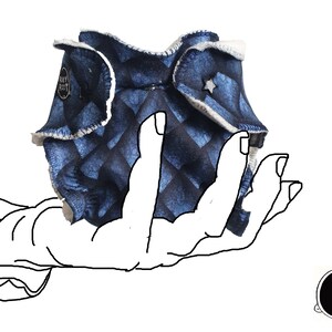 May include: A blue and white patterned cloth diaper with a white trim and a small star on the front. The diaper is folded and held in a hand.