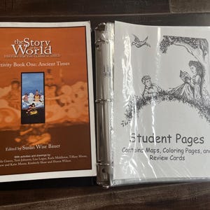 以下が含まれることがあります： スーザン・ワイズ・バウアー編集の「The Story of the World Activity Book One: Ancient Times」。中央にイラストが描かれたオレンジ色の表紙と、子供たちの白黒線画が印刷された学生用ページが入ったバインダーが並んでいます。