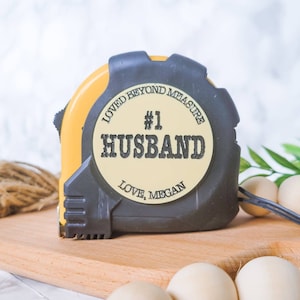 May include: A yellow and black measuring tape with a white sticker that says "Loved beyond measure #1 Husband Love, Megan".
