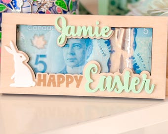 May include: A wooden money holder with a bunny cutout, a five dollar Canadian bill, and the words "Jamie Happy Easter" in green and gold lettering.