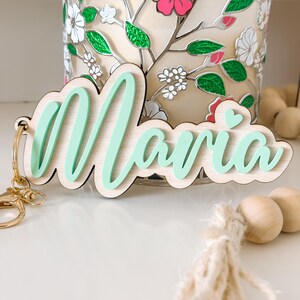 May include: A light green wooden keychain with the name "Maria" written in a cursive font. A small heart is included in the design.