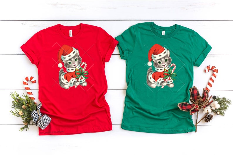 Puede incluir: Dos camisetas con un gatito navide&ntilde;o vintage que lleva un gorro de Pap&aacute; Noel y sostiene un bast&oacute;n de caramelo. La camiseta de la izquierda es roja y la camiseta de la derecha es verde.