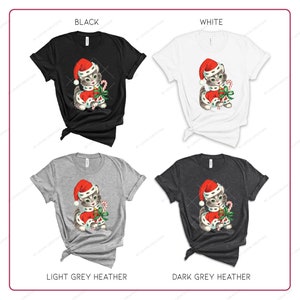 Puede incluir: Cuatro camisetas con un dise&ntilde;o de gato navide&ntilde;o. Las camisetas est&aacute;n en negro, blanco, gris claro jaspeado y gris oscuro jaspeado.